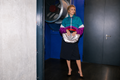 Woman in colourful windbreaker holding silver LUCY clutch, industrial space