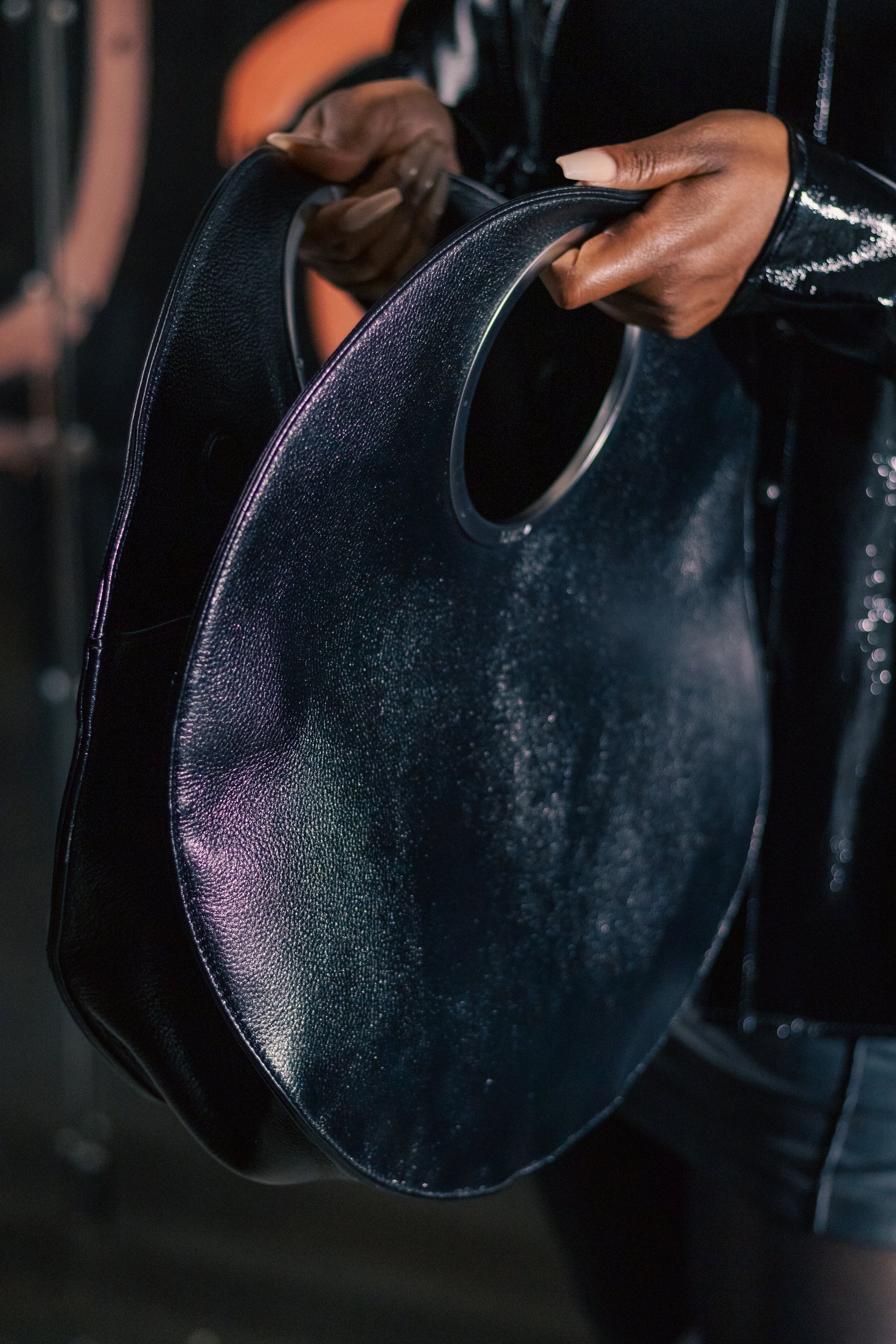 Iridescent Metallic Black bag held in hands, dark editorial setting