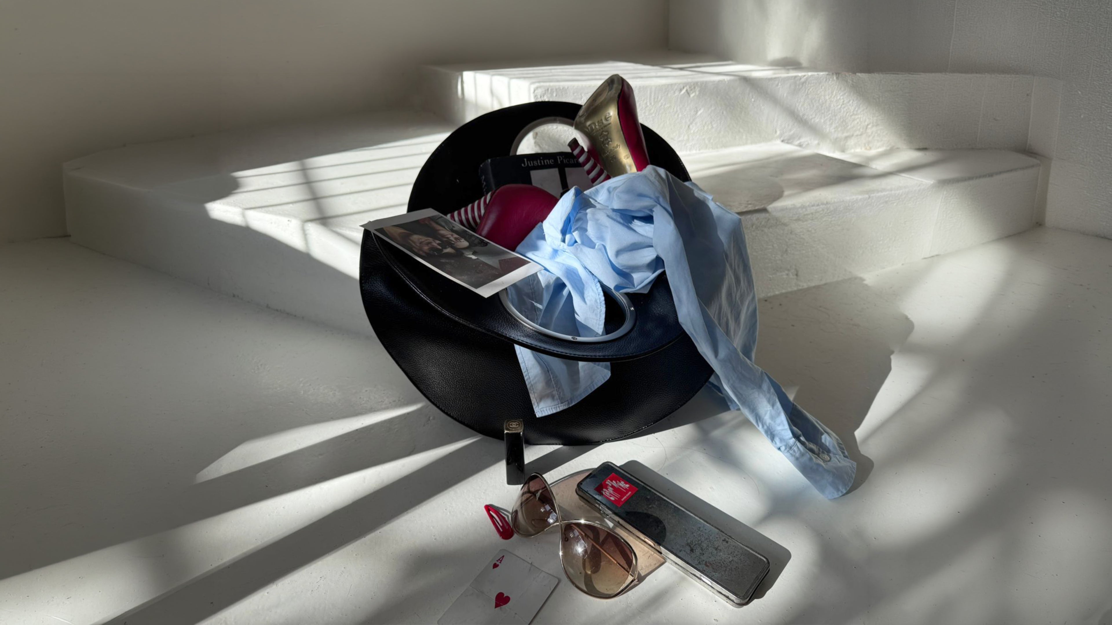 black Lucy bag on white steps, filled with magazines, blue shirt and a red heel